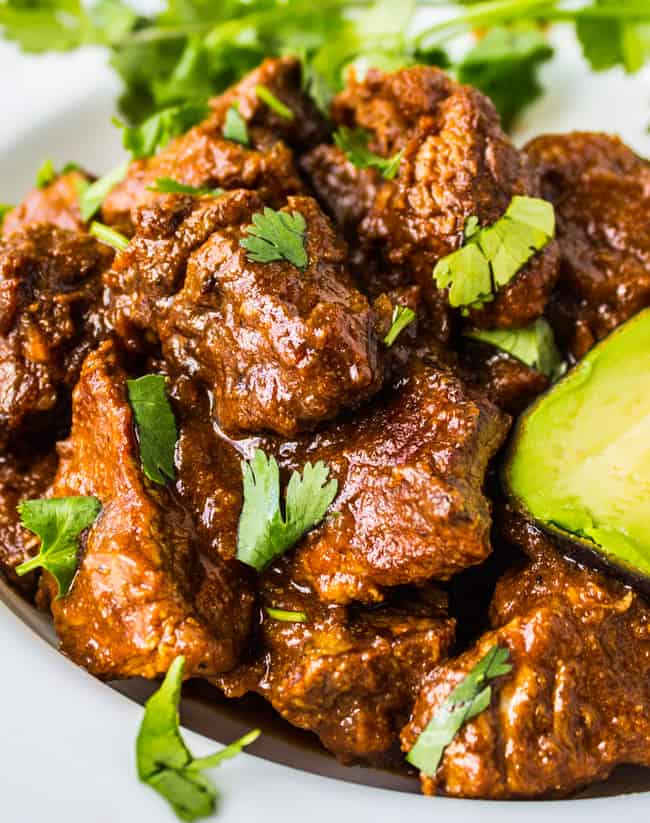 Tejano carne guisada with avocado and cilantro on a white plate.