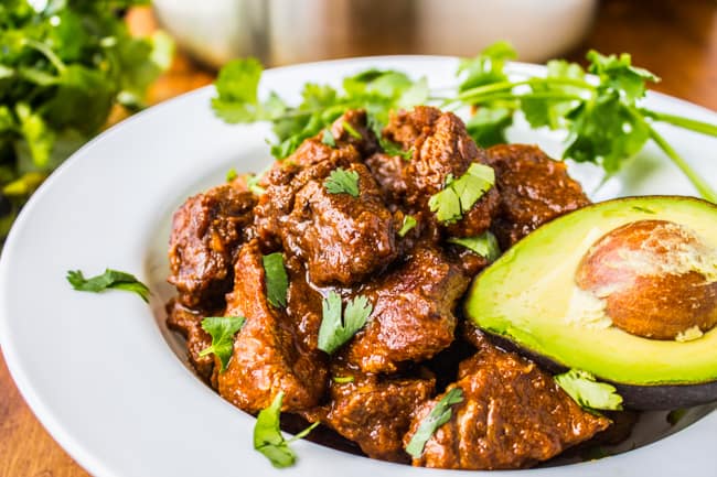 a white plate with carne guisada, half an avocado, and cilantro. 