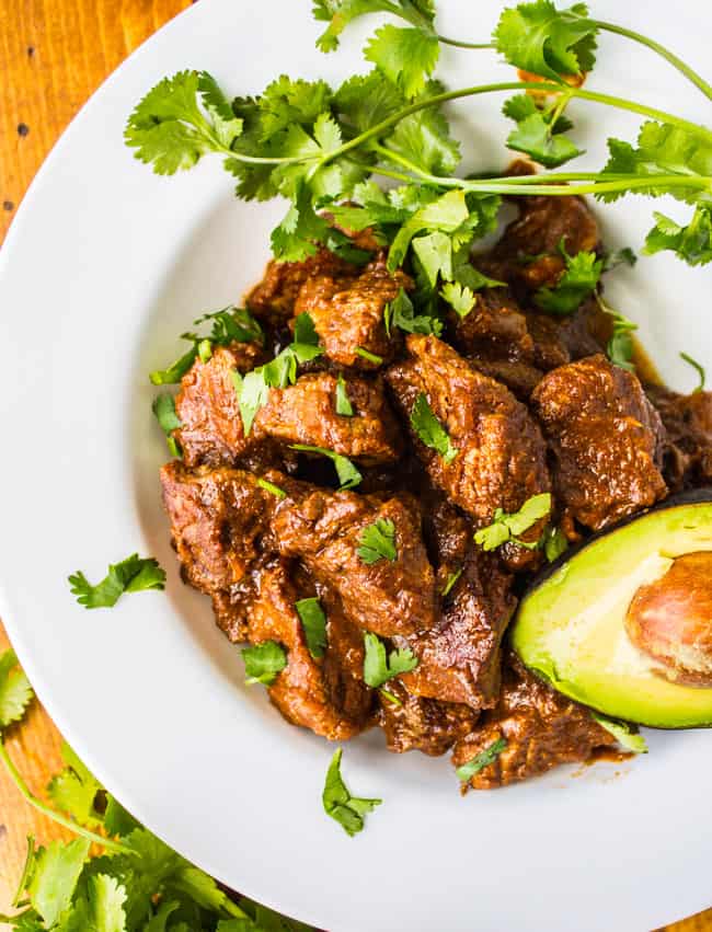 carne guisada in a white plate with cilantro and avocado. 