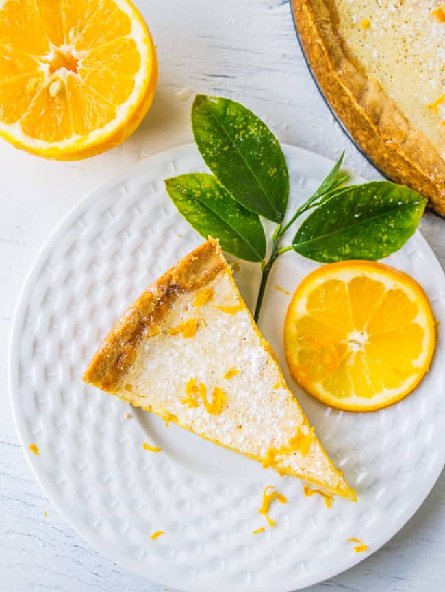 a slice of meyer lemon tart on a plate with lemon leaves and a meyer lemon slice. 