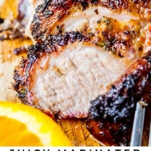 Close-up of juicy, sliced Cuban mojo pork on a wooden board, featuring crispy, marinated edges and tender meat, with a slice of orange and fresh herbs in the background. Text overlay reads: Juicy, Flavorful Cuban Mojo Pork.