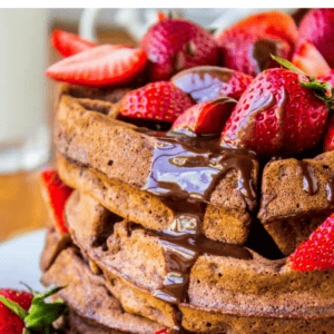 A stack of dark chocolate waffles topped with fresh strawberries and drizzled chocolate syrup.
