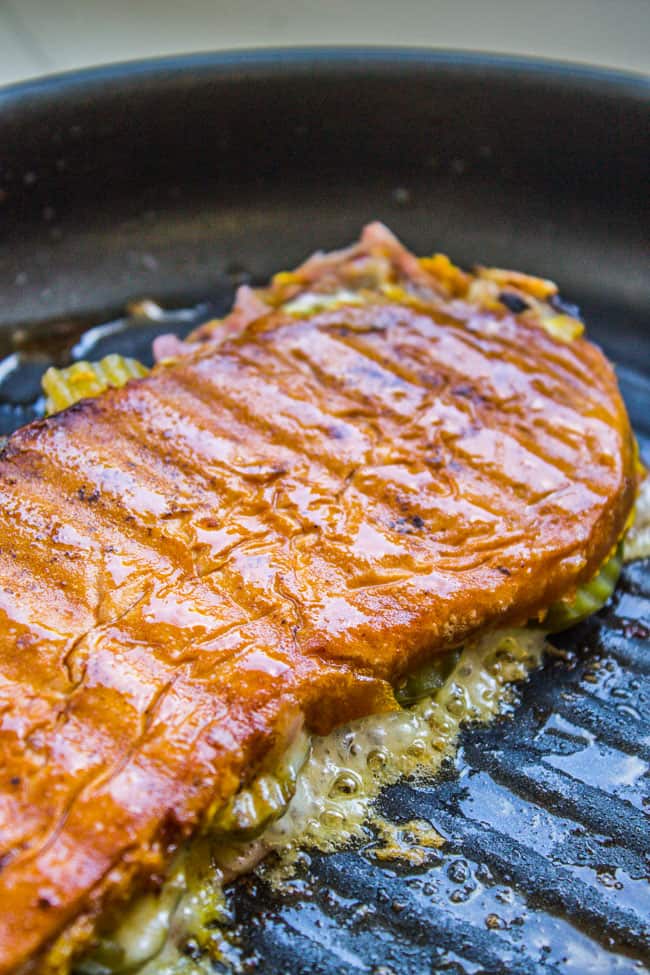 a cuban sandwich frying in a cast iron skillet.