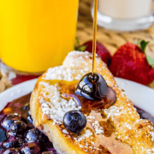 A slice of blueberry French toast casserole topped with powdered sugar, with syrup being poured over it.