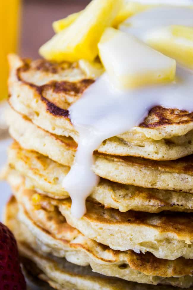 a stack of banana macadamia pancakes with homemade coconut syrup and fresh pineapple on top. 