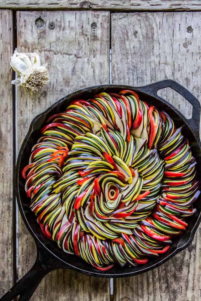 Ratatouille of sliced vegetables in iron pan on wooden table.