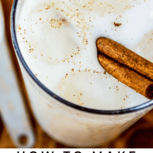 A glass of creamy vanilla bean horchata with ice cubes and a cinnamon stick, viewed from above. Text at the bottom reads: Vanilla Bean Horchata - The Food Charlatan.
