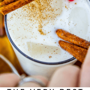 A glass of creamy vanilla bean horchata topped with ground cinnamon and two cinnamon sticks, featuring a red and white striped straw, labeled The Very Best Vanilla Bean Horchata - The Food Charlatan. Enjoy the classic flavor of vanilla bean in every sip.