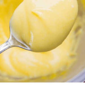 A spoonful of smooth yellow lemon curd held above a bowl, with text below reading Quick & easy lemon curd. The Food Charlatan.