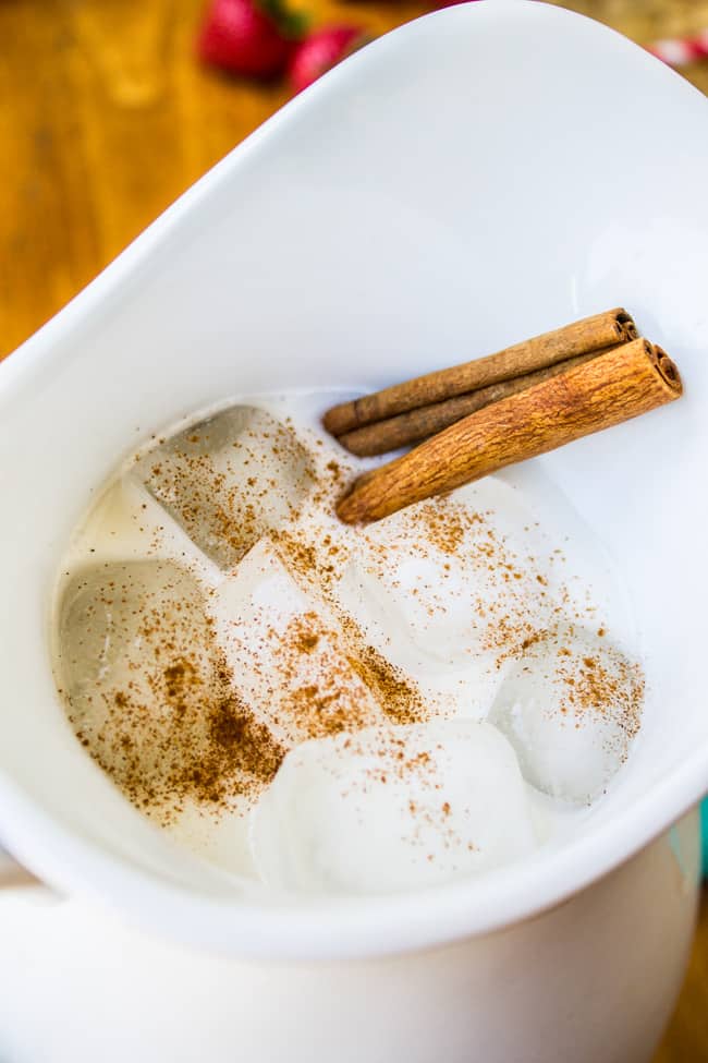 a white pitcher of horchata with cinnamon sticks and ice cubes.