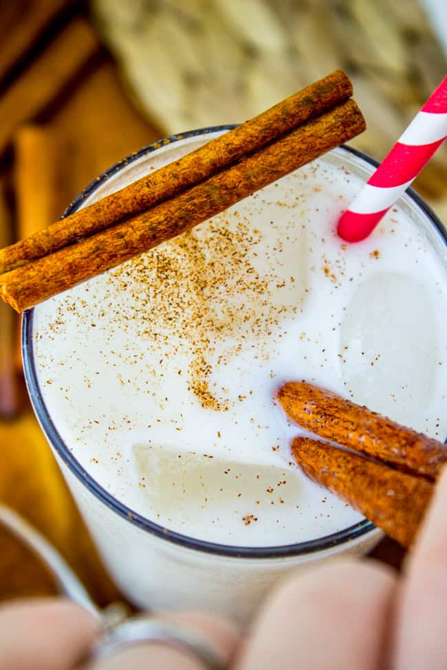 a tall glass of horchata with cinnamon sticks and a striped straw.