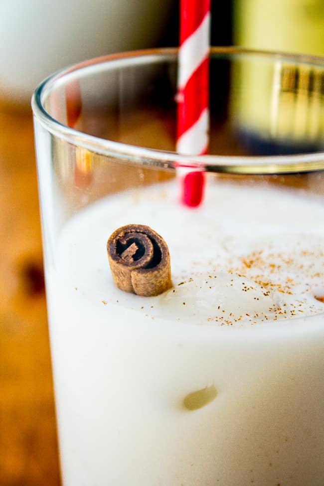 horchata in a glass with a striped straw and a cinnamon stick.