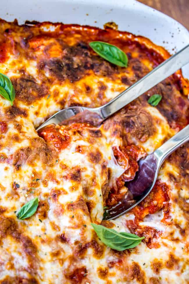 two metal spoons in a large pan of ravioli lasagna.