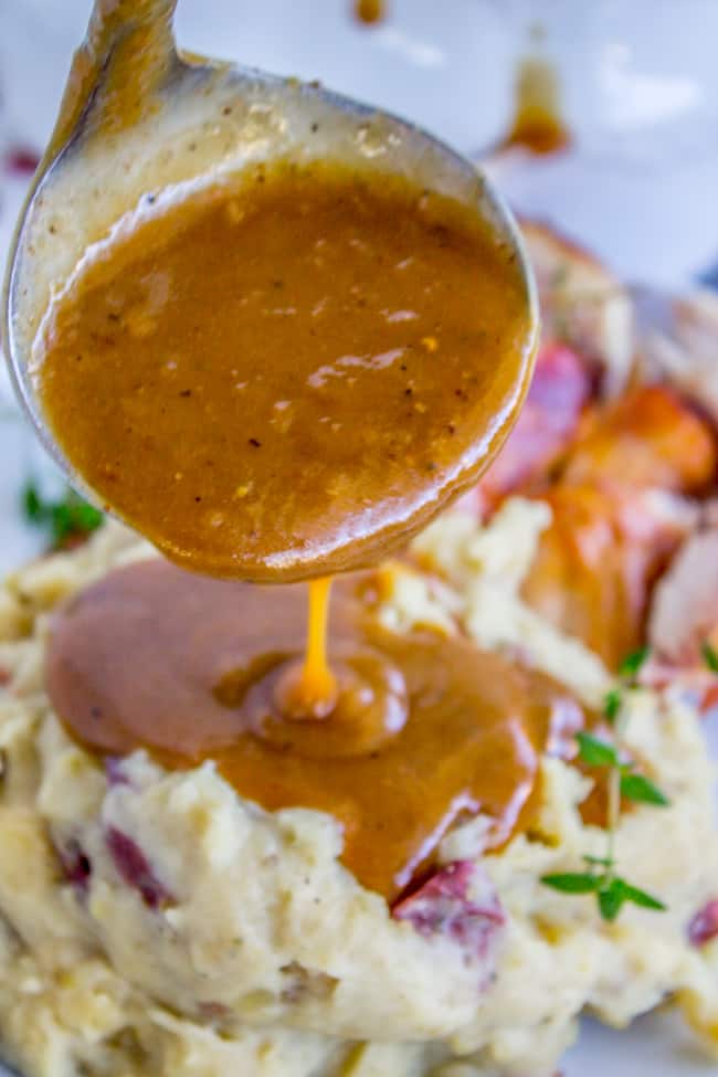 homemade turkey gravy poured from a ladle onto mashed red potatoes.