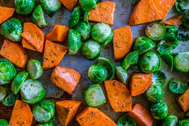 Raw, seasoned Sweet Potatoes and Brussels Sprouts on a chopping board