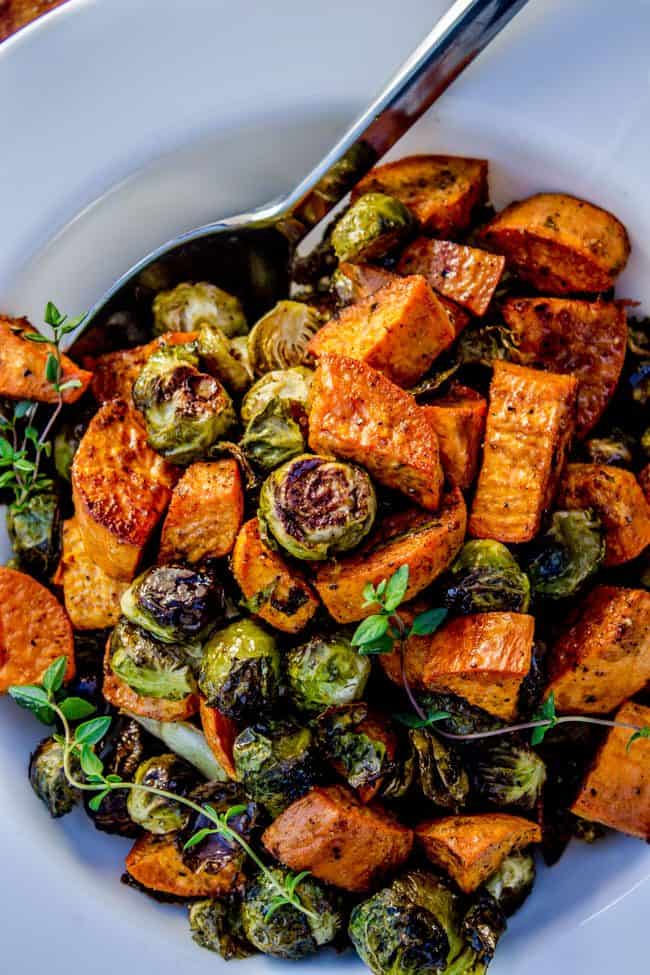 roasted sweet potatoes and Brussels sprouts in a white serving dish with a metal spoon. 