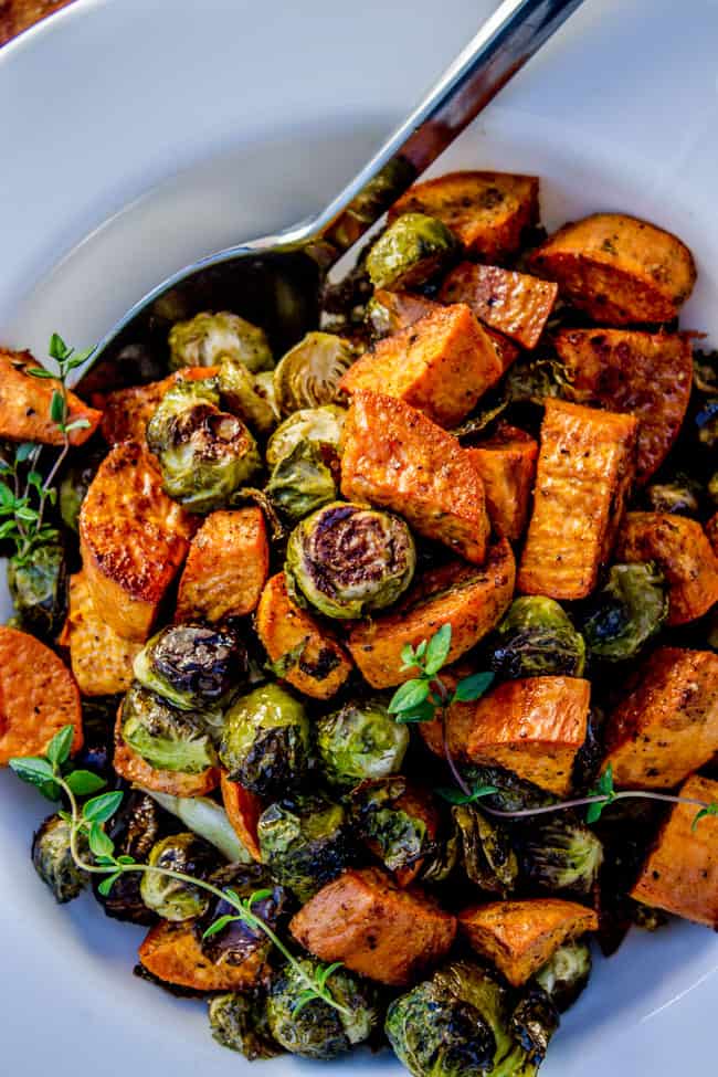 A spoon digging into roasted Sweet Potatoes and roasted brussels Sprouts from The Food Charlatan