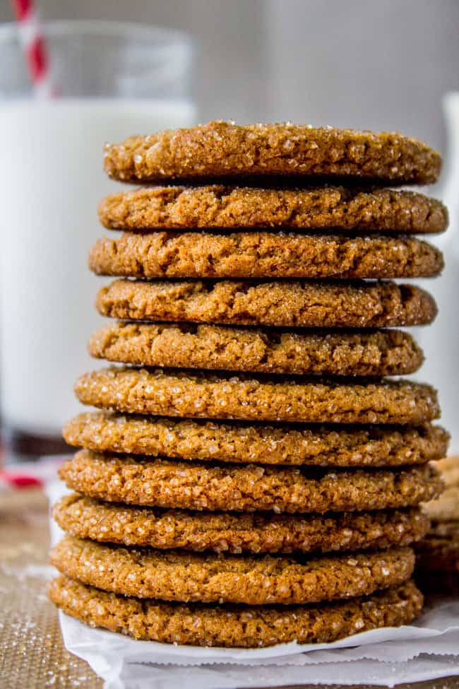 Straight stack of several gingersnap cookies with glass of milk in the background.