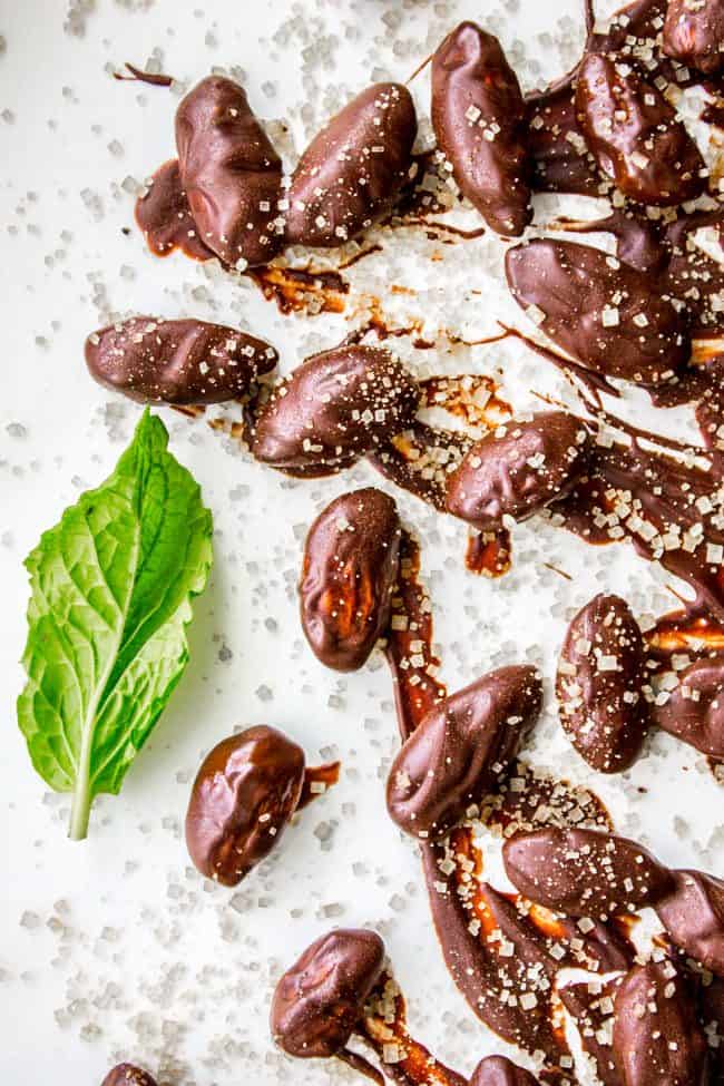 chocolate covered almonds with sea salt and a mint leaf on white parchment paper. 