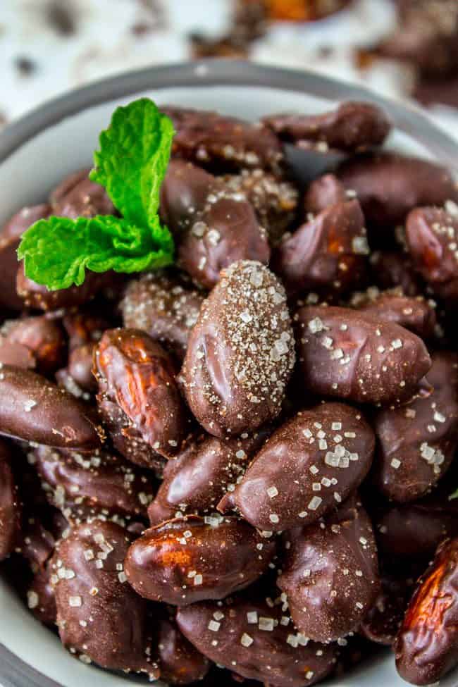 A white bowl filled with chocolate-coated almonds and a mint leaf. 