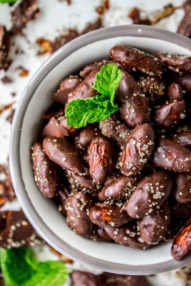 A white bowl filled with chocolate-coated almonds and a mint leaf. 