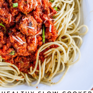 A close-up of spaghetti topped with chunky red meat sauce, grated cheese, and fresh basil sits beside a slice of bread on a white plate. Text below reads: Healthy Slow Cooker Spaghetti Meat Sauce - The Food Charlatan.