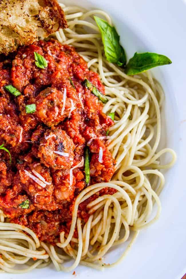 spaghetti sauce served over spaghetti with fresh basil and parmesan on a white plate.