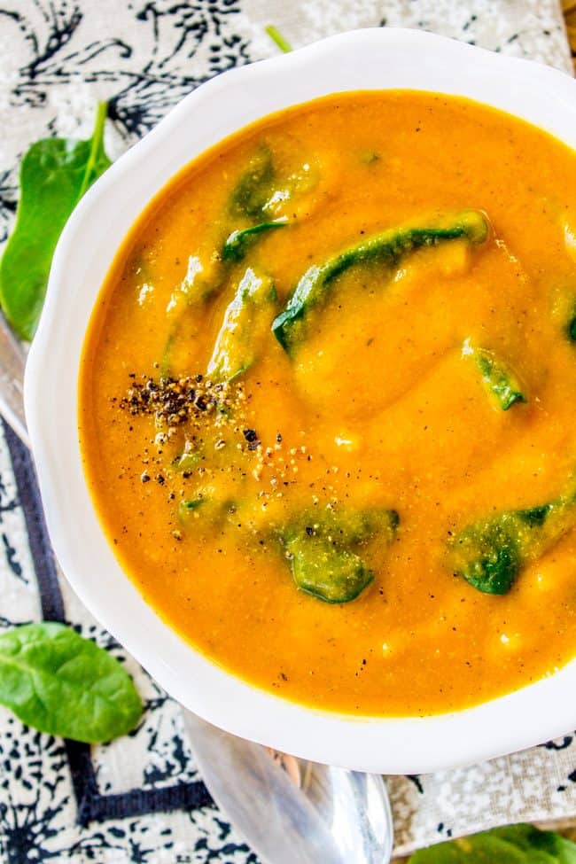 creamy vegan cauliflower soup with freshly ground pepper and spinach in a white bowl. 