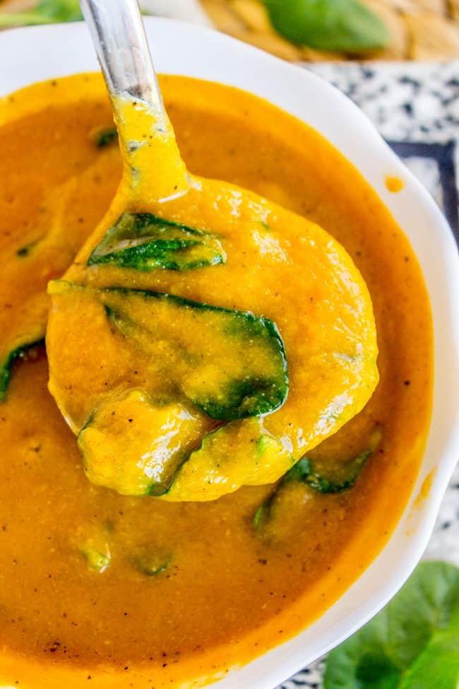 a spoonful of golden cauliflower soup with spinach in a white bowl.