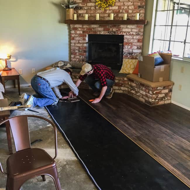 Two men laying down new hardwood flooring.