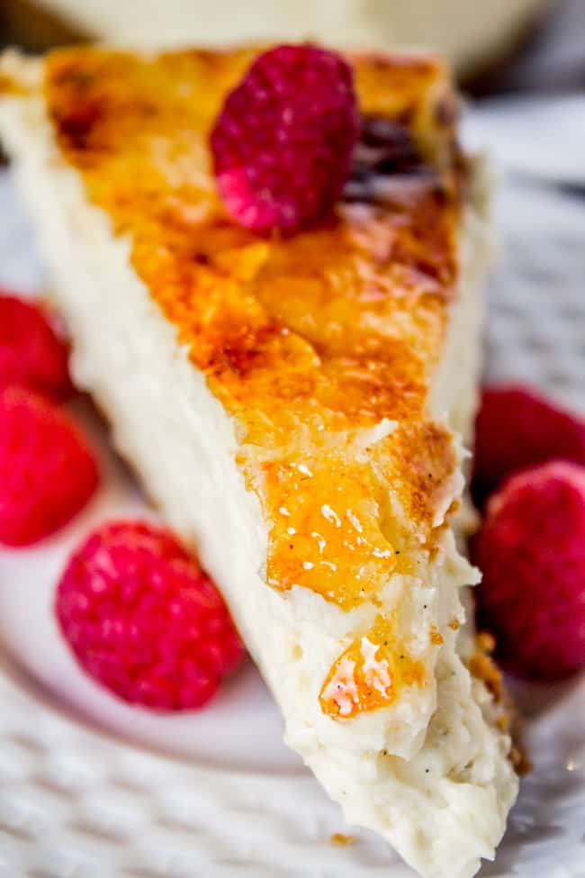 a piece of Crème Brûlée Cheesecake  with crackly top and fresh raspberries.