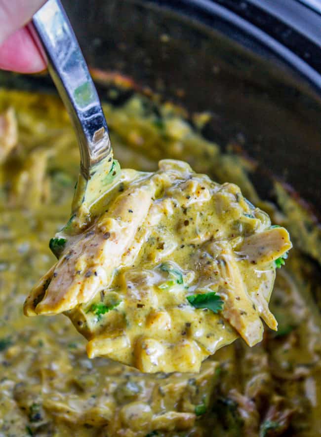 a serving spoon lifting chicken coconut curry from the crockpot. 