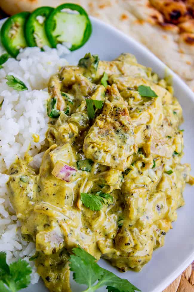 chicken coconut curry served with rice, naan, cilantro, and fresh sliced jalapenos on a white plate.