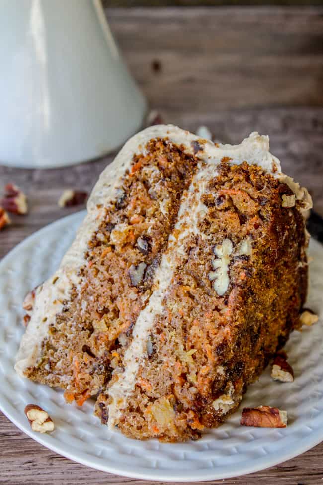 a slice of carrot cake with pecans and maple pecan cream cheese frosting on a white plate.