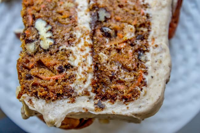 a close up shot of a slice of carrot cake with pecans and maple cream cheese frosting. 