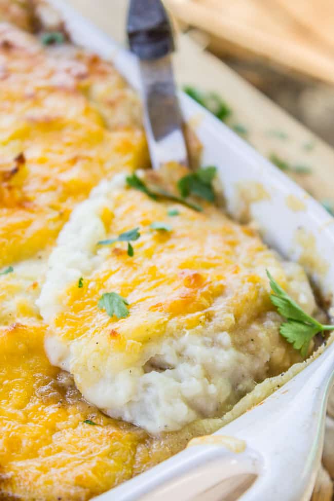 a large metal spoon in a pan of cheese-topped shepherd's pie.