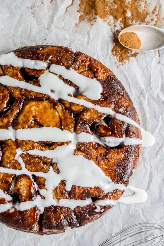 a round pan of cinnamon rolls turned out upside down onto parchment paper with icing drizzled on.