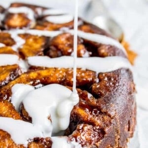 Icing being drizzled over a batch of freshly baked cinnamon rolls, highlighting their golden-brown, gooey texture and swirled, sugary layers from an easy cinnamon roll recipe.
