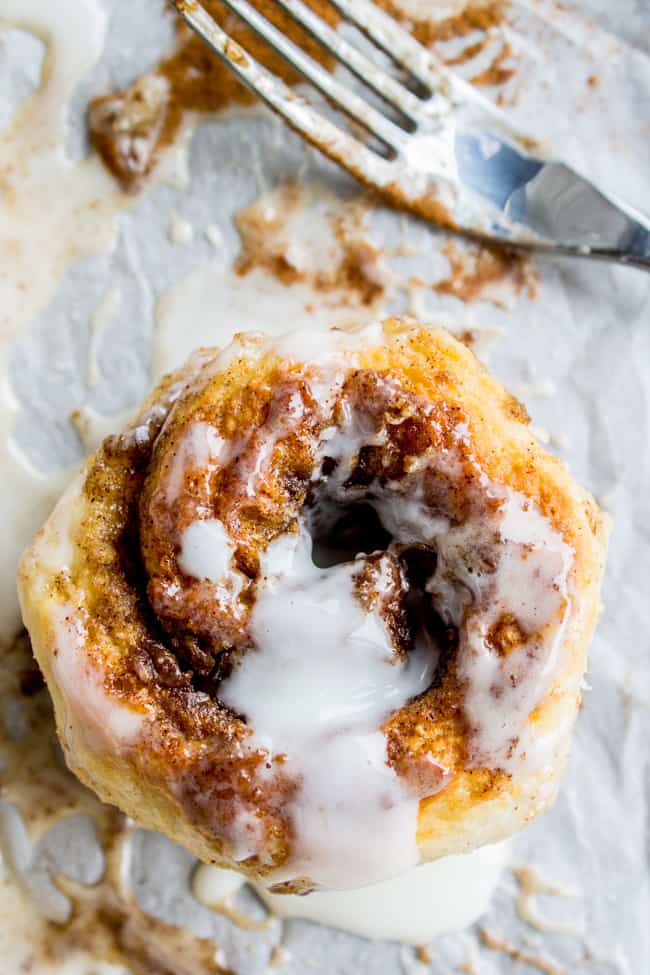a flaky cinnamon roll with icing on parchment with a fork nearby.