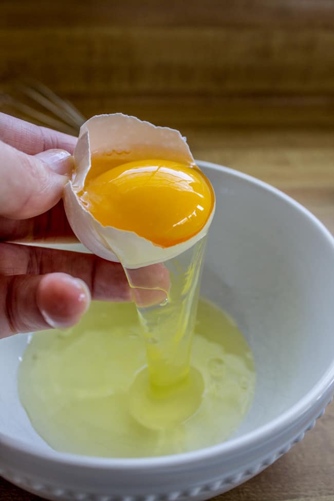 A hand separating the egg white from  the egg yolk.