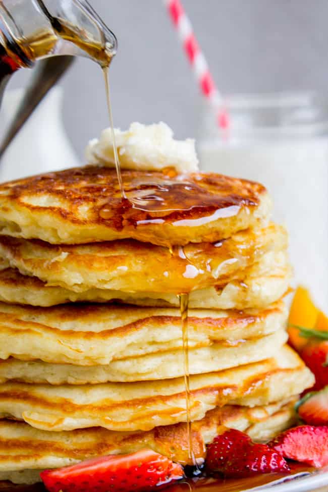 Pancakes stacked with butter on top and syrup running down the side and strawberries on the plate.