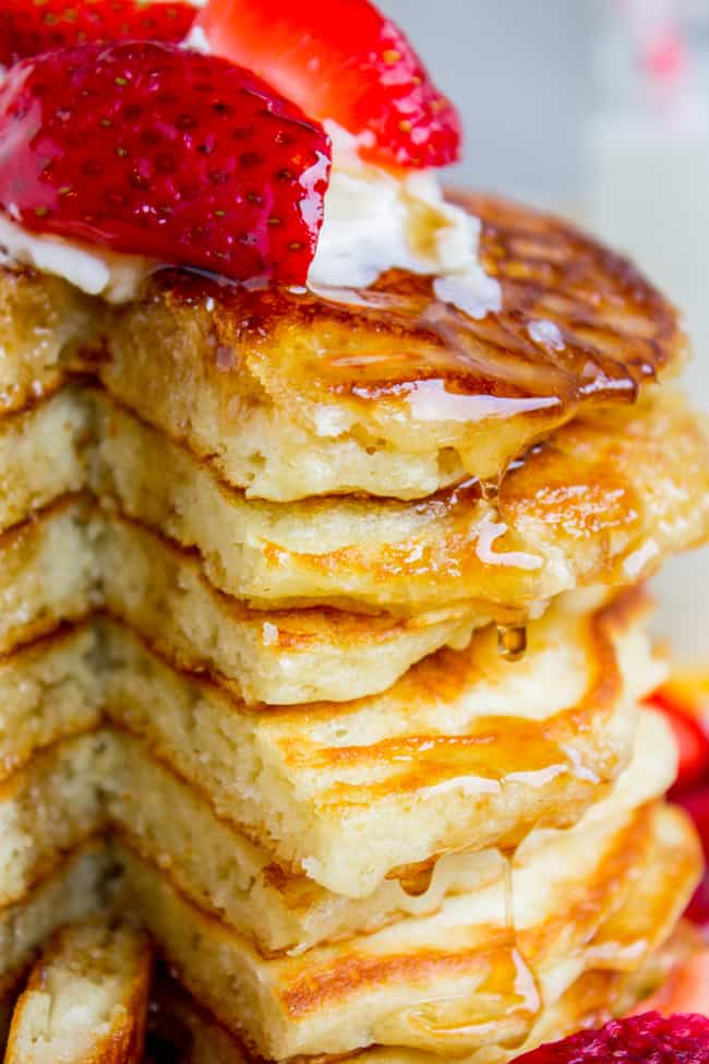 Delicious pancakes with syrup, strawberries, and butter on top, showing a stack of pancakes with a slice missing.