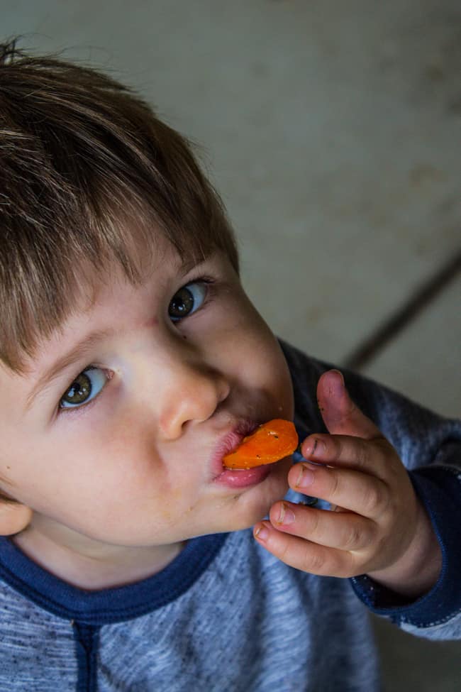 a little boy eating a sauteed carrot.