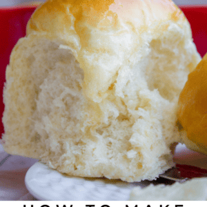 A close-up of a fluffy, golden-brown dinner roll being pulled apart, showcasing its soft, buttery texture. The image is labeled Buttery Dinner Rolls - The Food Charlatan.