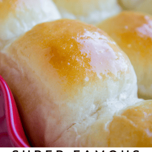Close-up of golden brown, shiny, freshly baked dinner rolls in a red baking dish. The fluffy texture shines through. Text at the bottom reads: Super Famous Buttery Dinner Rolls - The Food Charlatan.
