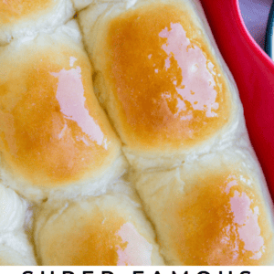 Close-up of six golden, shiny dinner rolls in a red baking dish. The rolls look soft and fluffy with a buttery glaze. Text reads Super Famous Buttery Dinner Rolls - The Food Charlatan, perfect for any dinner table.