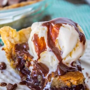 A slice of cookie pie topped with vanilla ice cream and drizzled with chocolate sauce on a white plate.