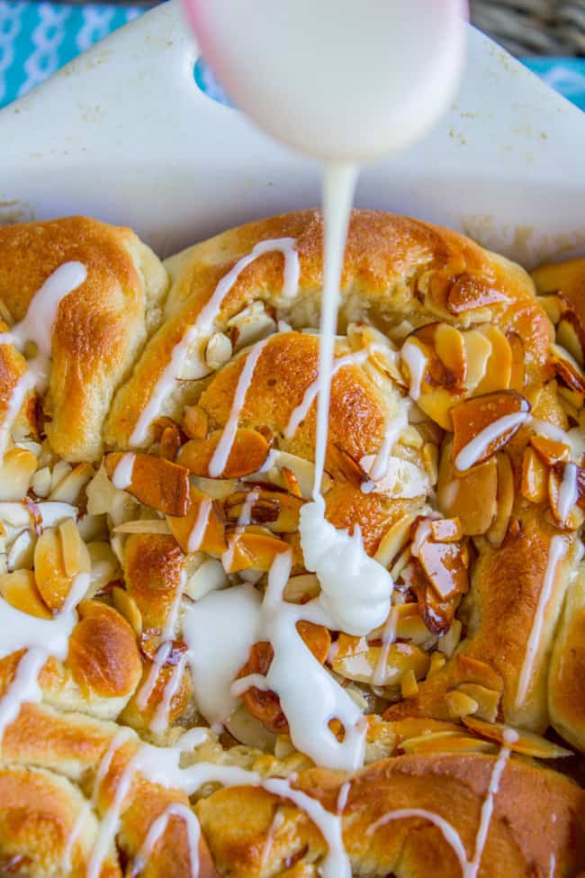 honey almond rolls with crunchy almond topping and glaze being drizzled on top. 