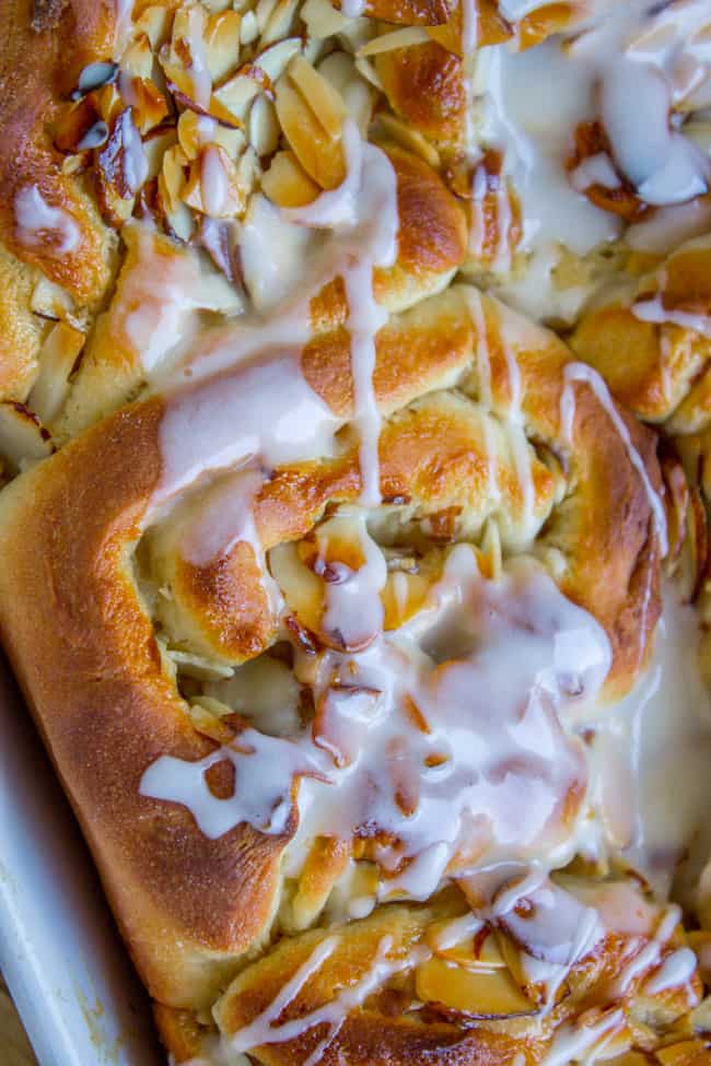honey almond rolls in a baking pan with glaze being drizzled on top. 