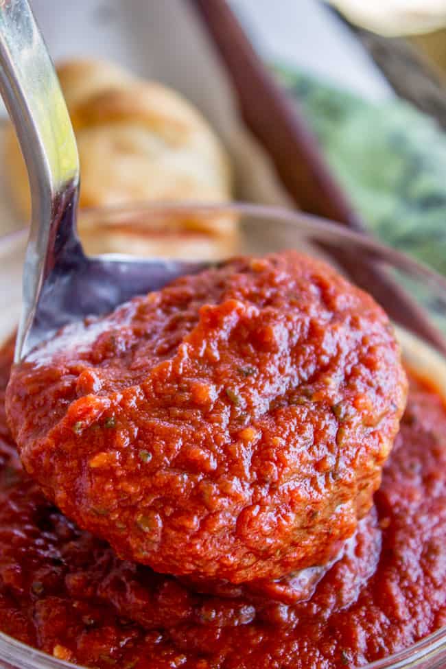 a ladle lifting pizza sauce from a glass bowl.